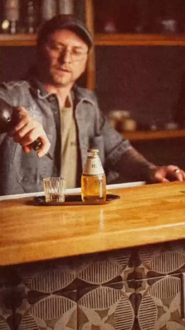 A bartender in a denim jacket pours behind a wooden bar