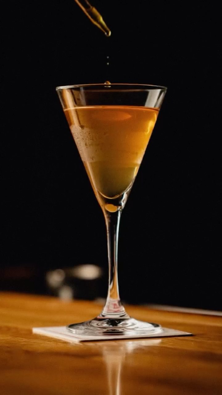 An amber cocktail in a martini glass, a single drop falling in