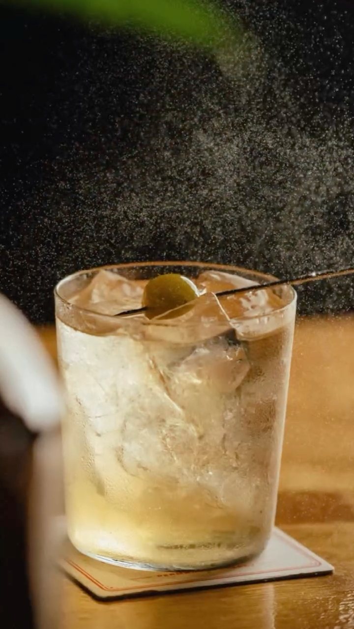 A highball with an olive and a fine mist in the air