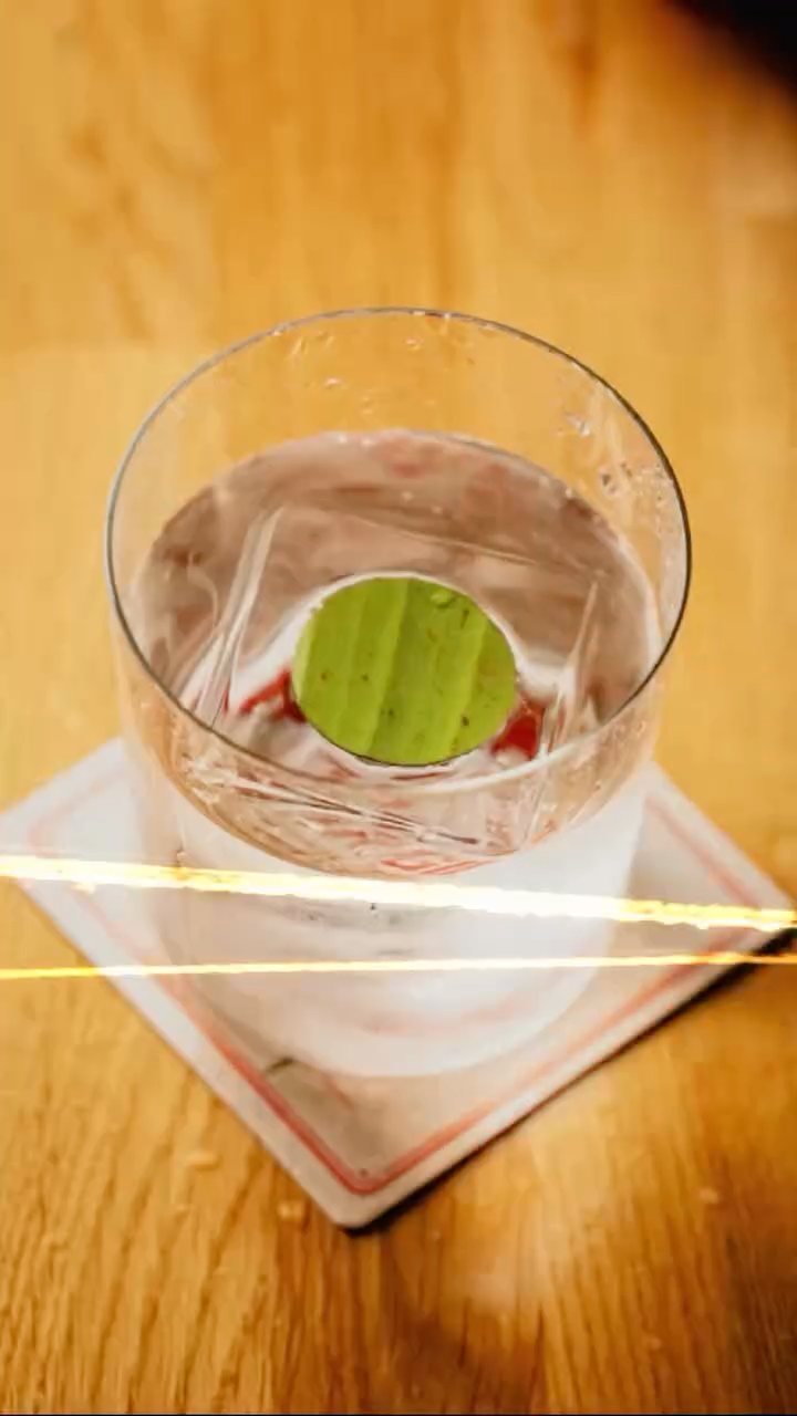 A clear drink with a lime wheel on a coaster