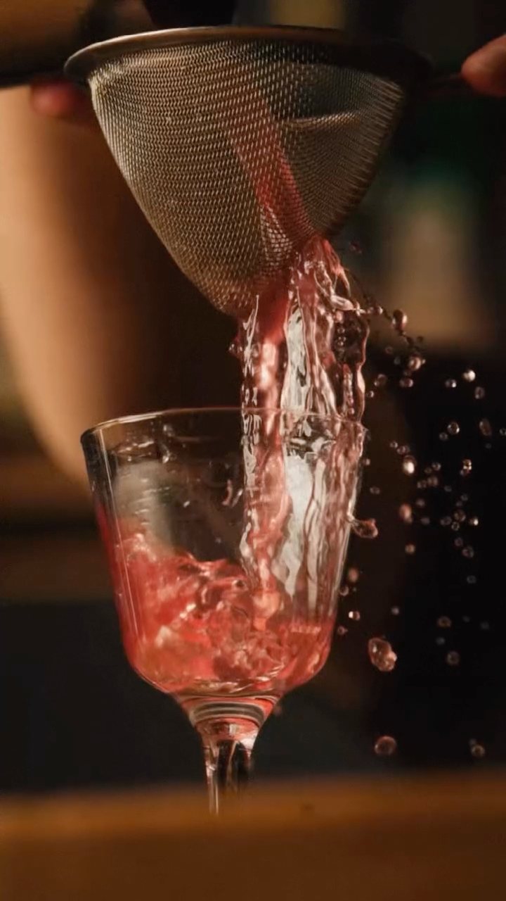 A pink cocktail strained into a glass mid-pour